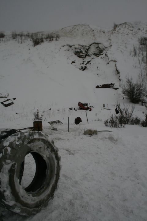 2003 Jeep TJ - A snowy landscape with a large tire in the foreground and various pieces of debris scattered across the hillside.