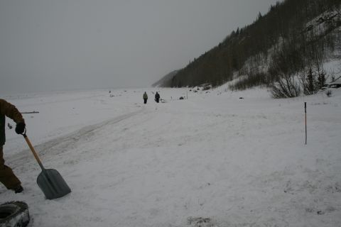 2003 Jeep TJ - A winter scene with people working in the snow near a wooded hillside and a frozen body of water.