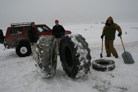 2003 Jeep TJ - People and large tires are gathered around a red SUV in a snowy Kincaid Park during a tire clean-up event.