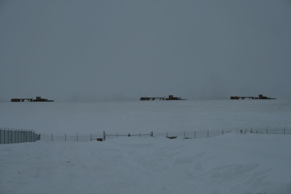 Three yellow industrial machines sit on a snow-covered plain under a gray sky