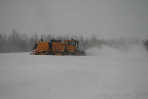 2003 Jeep TJ - A yellow snow blower is seen clearing snow in a field with trees in the background.