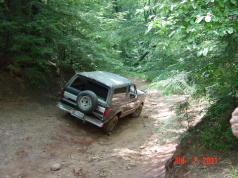 1995 Ford Bronco - Elevated rear three-quarter view of a two-tone brown-over-tan full-size Ford Bronco with a mud-caked lower body, angled off-camber on a dir…