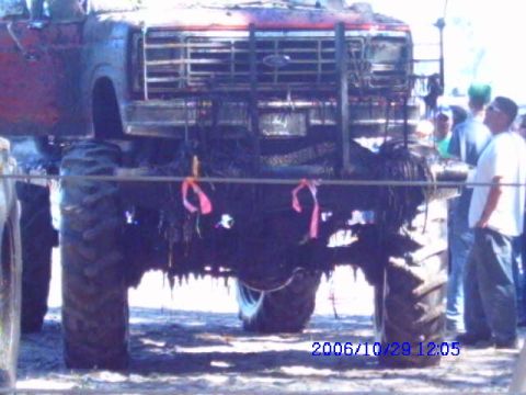 1987 Suzuki Samurai - A heavily modified truck with oversized tires is seen from the front, with people standing nearby.