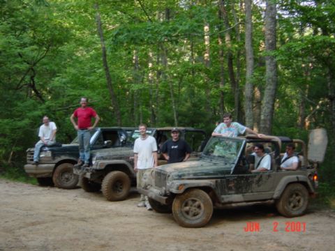 1995 Ford Bronco - Group photo of seven people posed with three mud-covered 4x4s parked on a dirt forest road, including a green Jeep Wrangler with the soft t…