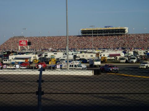 2000 Ford E350 - A busy parking area at a race track with numerous vehicles and spectators filling the stands.