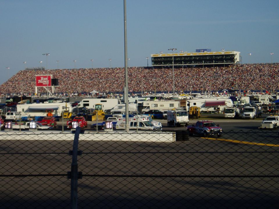 Parking lot scene with RVs, trucks, and ambulances in front of a crowded grandstand