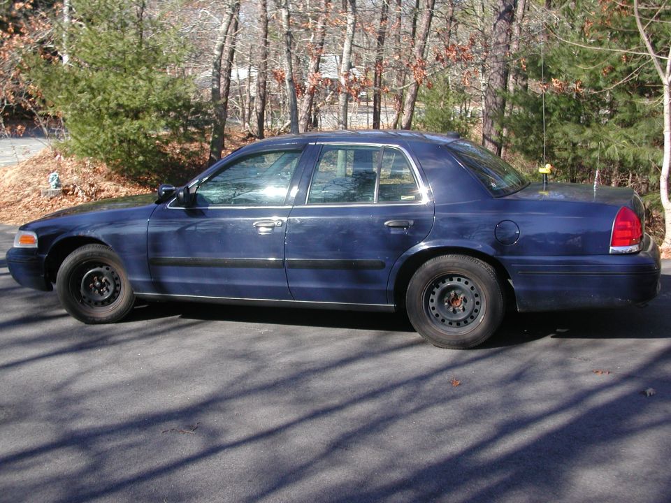 Side view of a dark blue sedan parked on asphalt, with trees in the background