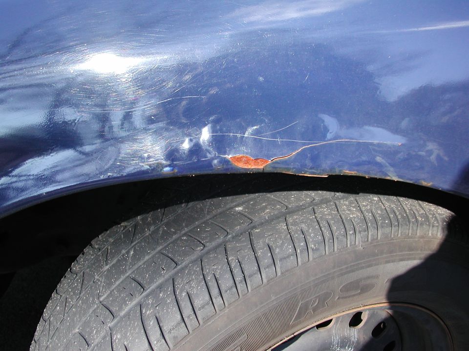 Close-up of a blue car's fender showing scratches and rust near the wheel well