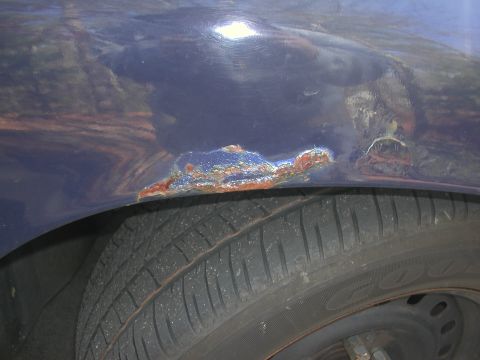 1999 Ford Crown Victoria - Rust damage is visible on the fender of a dark blue vehicle, with a tire in the foreground.
