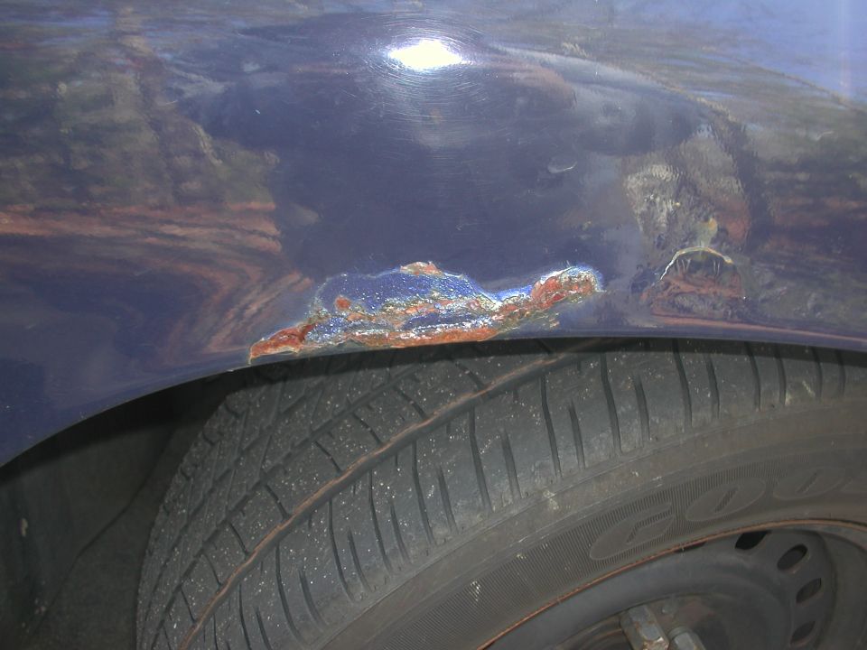 Dark blue car fender with significant rust and bubbling paint near the wheel well
