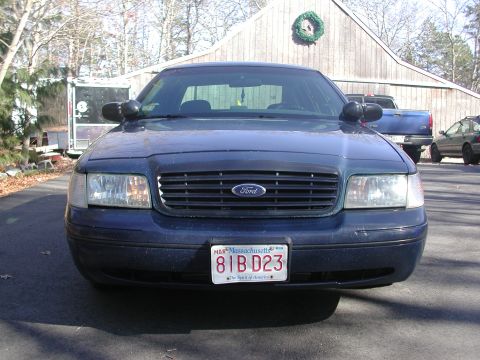 1999 Ford Crown Victoria - Front view of a dark blue 1999 Ford Crown Victoria parked in front of a wooden building.