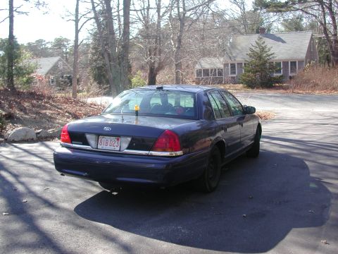 1999 Ford Crown Victoria - The sedan has a chrome strip above the license plate and a yellow object on the roof.
