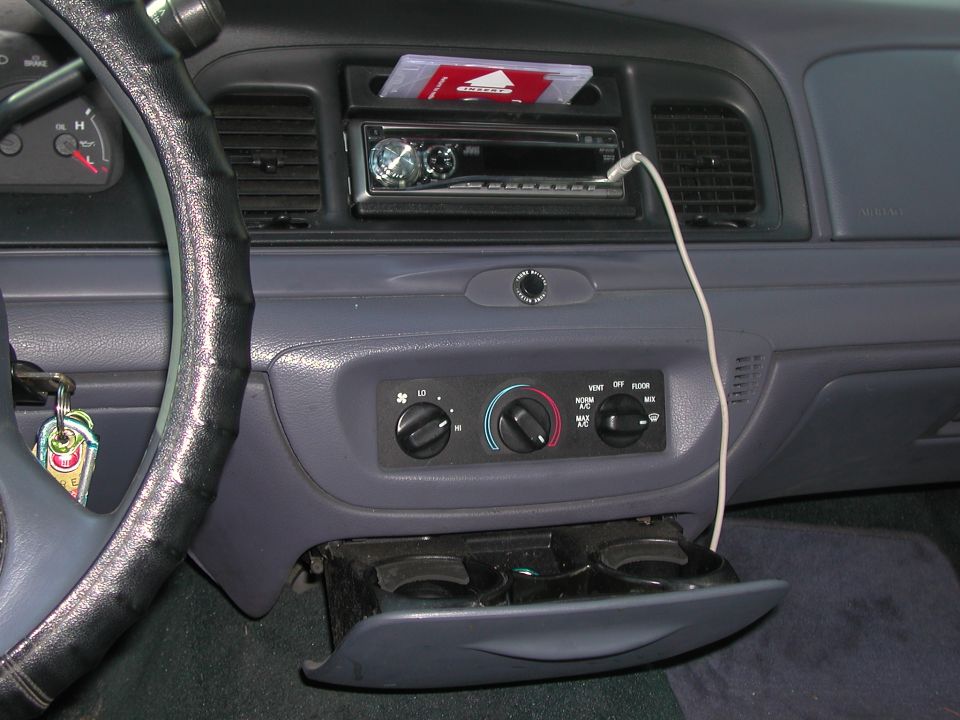 Car dashboard with steering wheel, radio, and climate controls. Cup holder is open