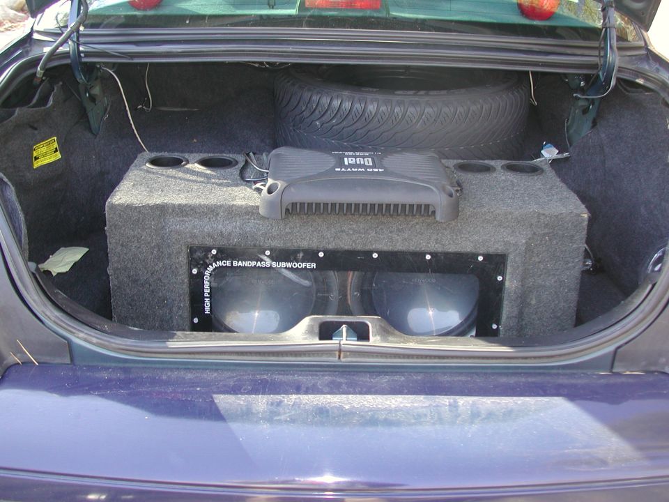 Dark blue 1999 Ford Crown Victoria trunk interior with a large subwoofer box, two subwoofers, an amplifier, and a spare tire