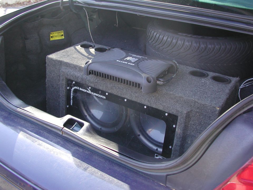 Car trunk interior showing a dual subwoofer box, a DUAL 480 watt amplifier, and a spare tire