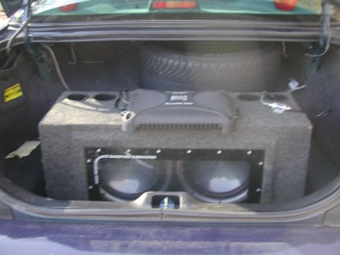 1999 Ford Crown Victoria - The trunk of a car contains a large subwoofer box with two speakers and an amplifier, along with a spare tire.