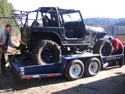 1989 Ford Bronco - A black Jeep Wrangler is loaded onto a trailer, ready for transport, with two men securing it.