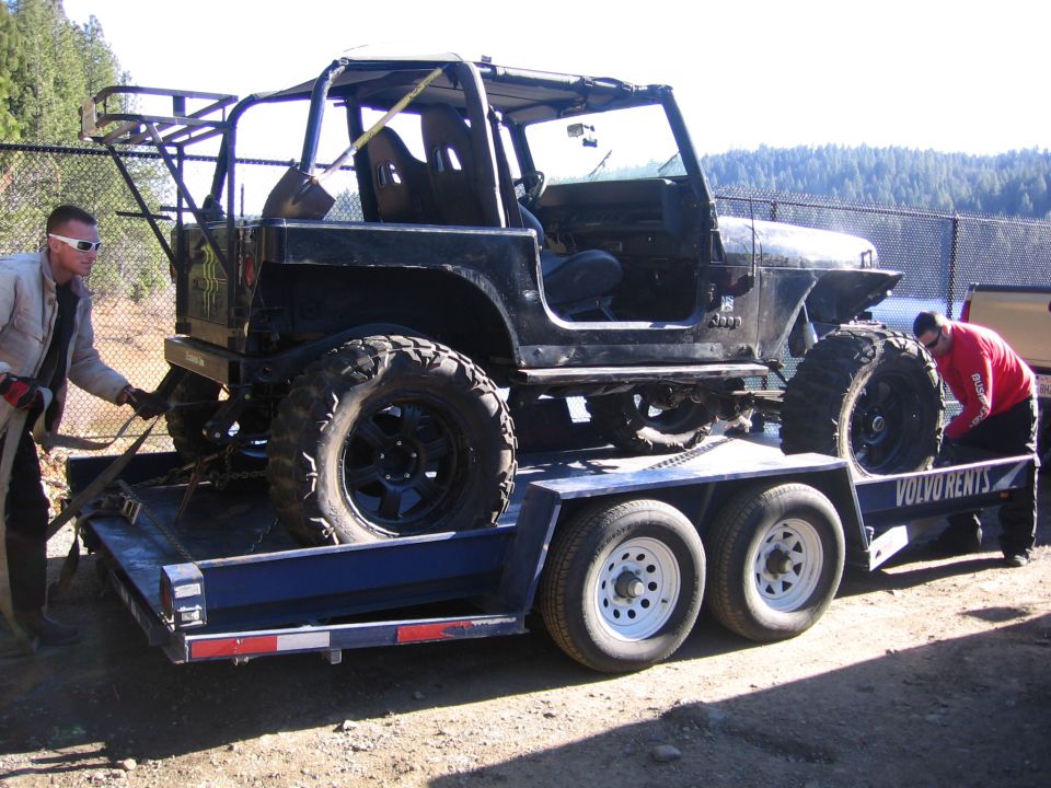 Black Jeep Wrangler on trailer, side view, with large off-road tires