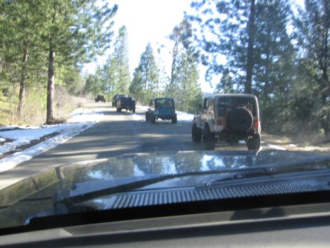 1989 Ford Bronco - A convoy of Jeeps drives down a tree-lined road with snow on the shoulders.