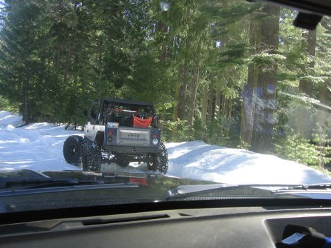 1989 Ford Bronco - A lifted Jeep Wrangler navigates a snow-covered path through a dense forest.