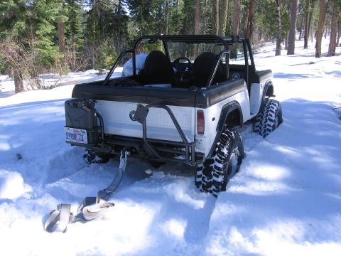 1989 Ford Bronco - A white 1989 Ford Bronco equipped with a roll cage and auxiliary fuel can is stuck in the snow during an off-road excursion.