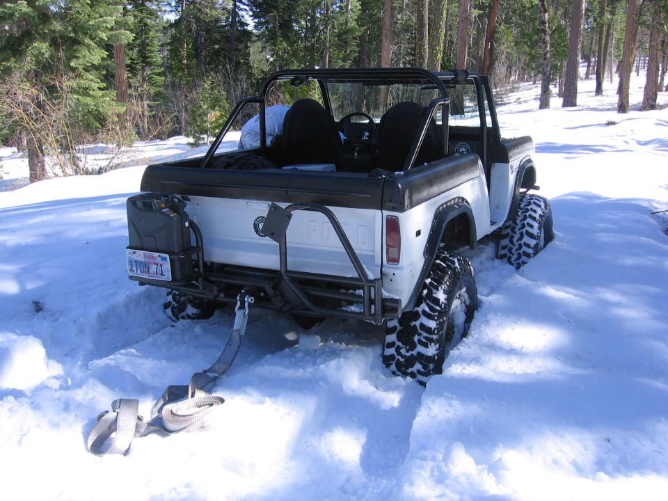 White 1989 Ford Bronco with roll cage stuck in snow, rear view