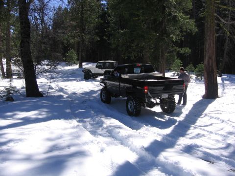 1989 Ford Bronco - Two off-road vehicles are parked on a snow-covered trail surrounded by trees.