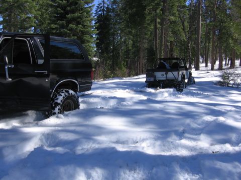 1989 Ford Bronco - A black 1989 Ford Bronco navigates a snowy trail with its door ajar, while another off-road vehicle follows in the distance.