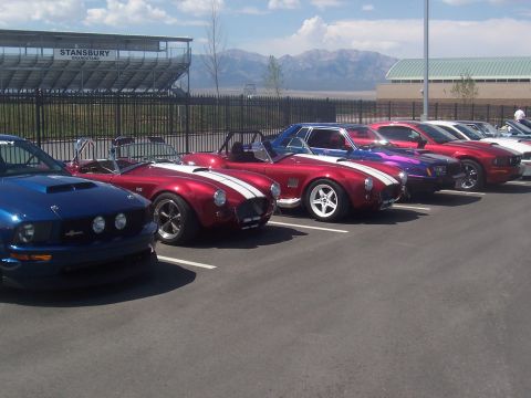 1973 Ford Mustang - A row of sports cars are parked in a lot, with mountains in the distance.
