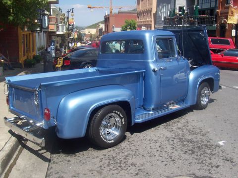 1973 Ford Mustang - A blue pickup truck is parked on a street with other vehicles and buildings in the background.