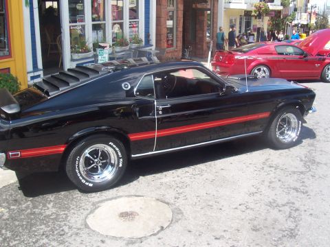 1973 Ford Mustang - Black 1969 Ford Mustang with red stripe parked on street next to a red Ford Mustang.