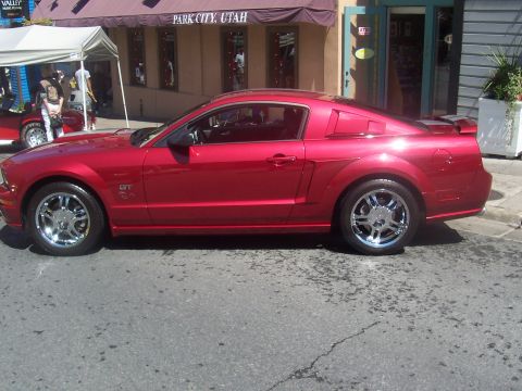1973 Ford Mustang - A red Ford Mustang is parked on a street in front of a building with 'Park City, Utah' signage.