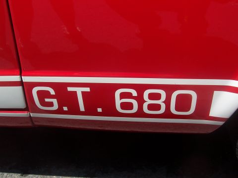 1973 Ford Mustang - Close-up of a red car's side panel showing a white stripe and 'G.T. 680' lettering.
