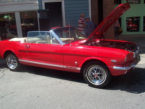 1973 Ford Mustang - Classic red convertible parked on street with hood open, showing engine bay. Likely a 1965 Ford Mustang.