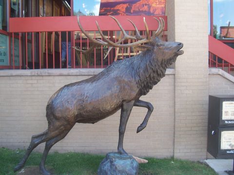 1973 Ford Mustang - A bronze elk statue stands on a rock in front of a building with red railings and brick walls.