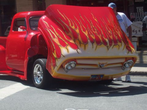 1973 Ford Mustang - A custom red pickup truck with a flame paint job is displayed with its hood open.