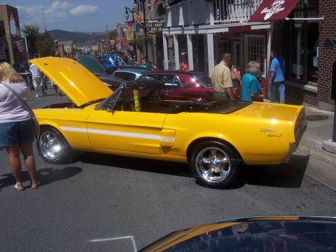 1973 Ford Mustang - Yellow 1968 Ford Mustang convertible parked on a street with other cars and people.
