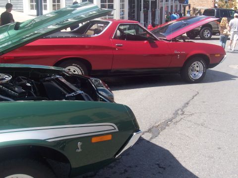 1973 Ford Mustang - Two classic cars, a red Ford Ranchero and a green car, are parked on a street with their hoods open.