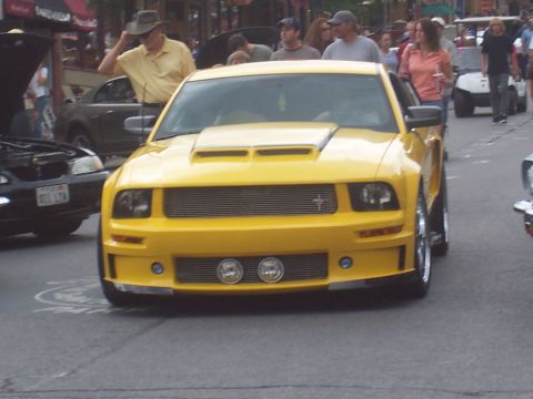 1973 Ford Mustang - A yellow Ford Mustang is parked on a street, with other vehicles and people around.