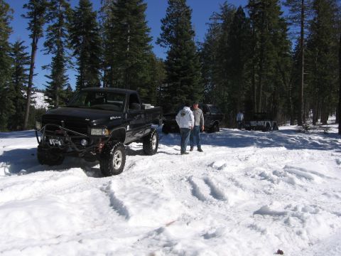 1989 Ford Bronco - Modified black Dodge Ram pickup truck parked in snow with other vehicles and people nearby.