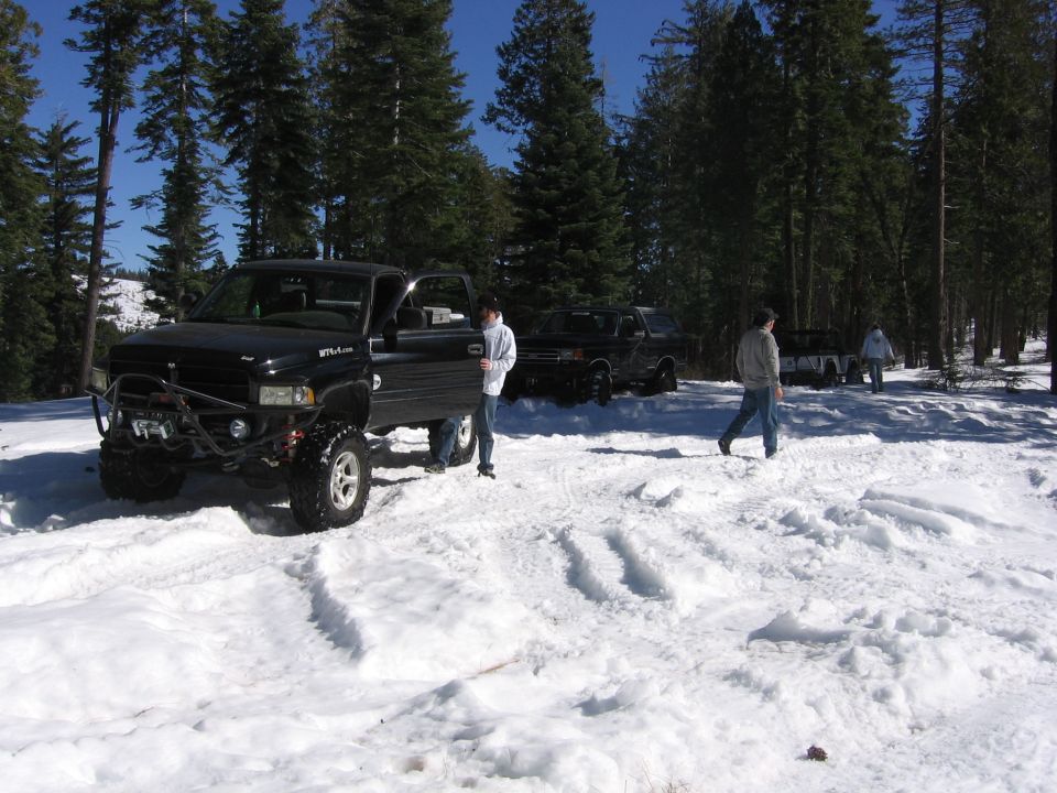 Black pickup truck with off-road tires and winch in snow, other trucks and people around