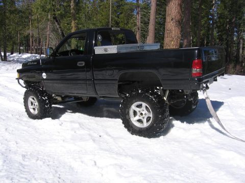 1989 Ford Bronco - A lifted black pickup truck sits in a snowy forest clearing.