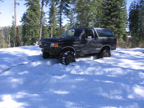 1989 Ford Bronco - This black SUV navigates a snowy terrain, its lifted suspension clearly visible as it powers through the deep snow.