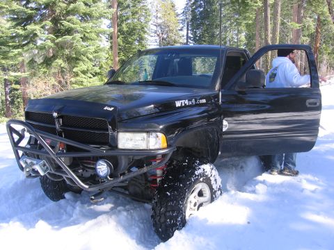 1989 Ford Bronco - A black pickup truck with large tires is stuck in deep snow, with the driver's door open.