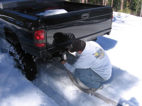 1989 Ford Bronco - Man attaches tow strap to a black pickup truck stuck in deep snow.