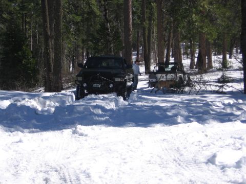 1989 Ford Bronco - Two off-road vehicles navigate a snow-covered path through a dense forest.