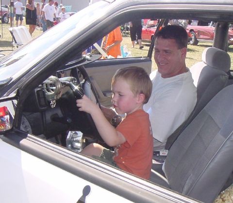 1993 Ford Mustang - A young boy pretends to drive a 1993 Ford Mustang while a man watches him from the passenger seat.