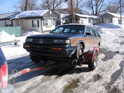 1999 Ford Taurus - A dark blue station wagon with wood paneling is being towed on a U-Haul trailer through a snowy area.