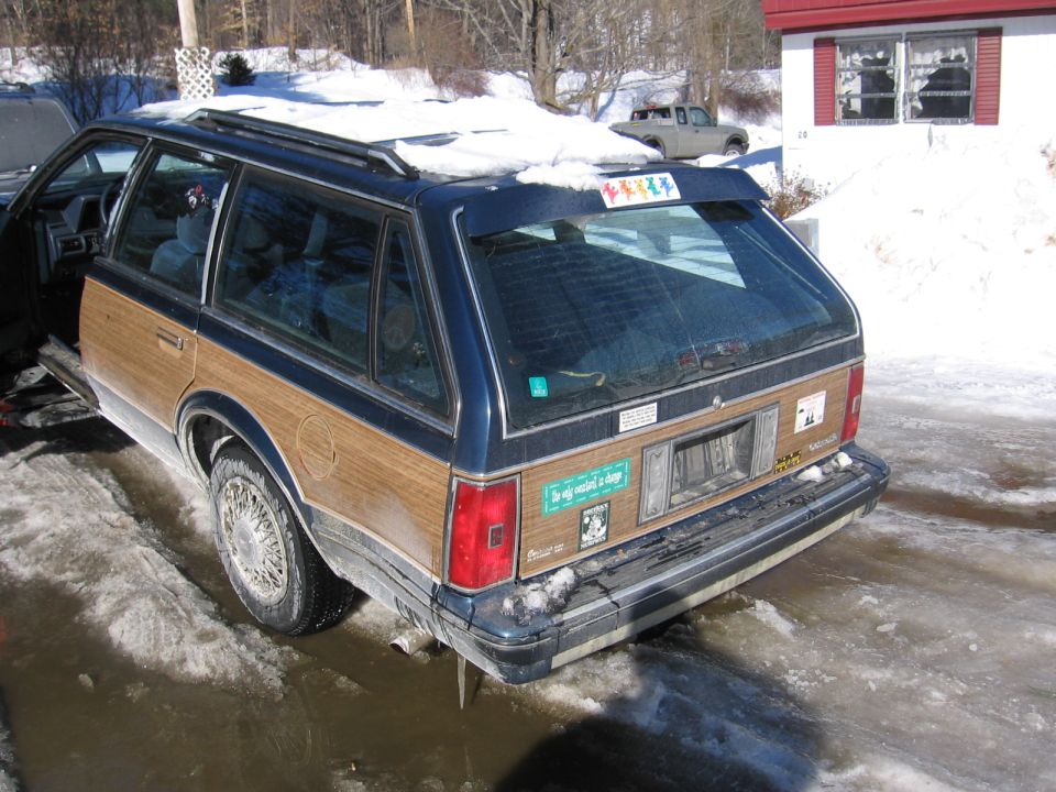 Wood-paneled station wagon in snow, rear view. License plate area is empty