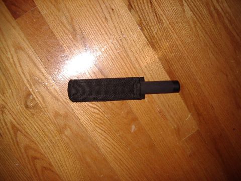 1985 Ford Bronco - A black expandable baton rests on a wooden floor, partially covered by its sheath.